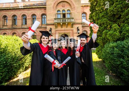 Bonne journée de remise des diplômes. 5 diplômés tiennent ses diplômes de deuxième cycle entre leurs mains. Banque D'Images