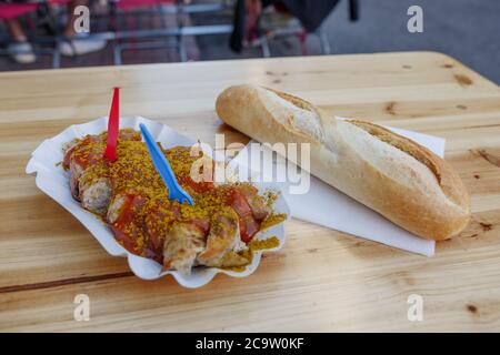 Currywurst, saucisse de porc grillée sur le dessus avec poudre de curry, servie avec une sauce au ketchup au curry sur une assiette de papier blanc, et pain français à la baguette. Banque D'Images