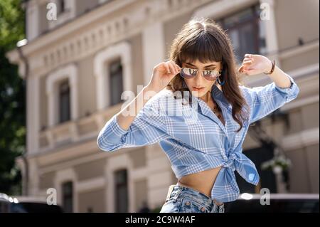 Portrait extérieur de yong belle femme souriante portant des lunettes de soleil élégantes, blouse à pois noirs, jeans de maman bleu, avec petit sac matelassé. Mod Banque D'Images