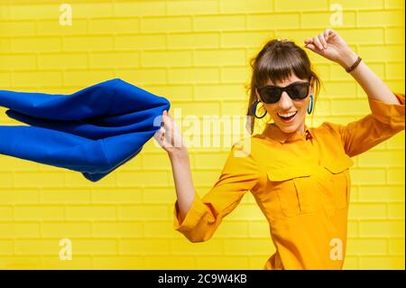 Gaie fille branplats une veste bleue contre le mur jaune. Une fille heureuse aux couleurs vives aime la vie. Banque D'Images