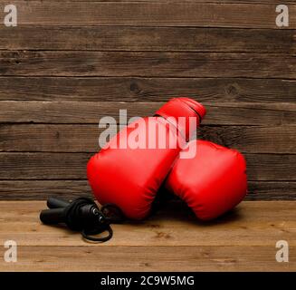 Deux gants de boxe rouges reposent sur un fond marron en bois, corde sautant l'espace vide Banque D'Images