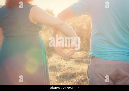 Femme enceinte et son mari regardant le coucher du soleil et tenant leurs mains en forme de coeur. Gros plan. Famille, grossesse, concept d'amour, fond, mur