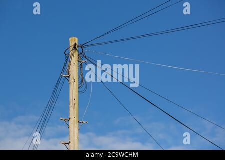 Lignes téléphoniques sur un poteau en bois ou un poteau télégraphique dans une rue se dirigeant vers différentes maisons Banque D'Images