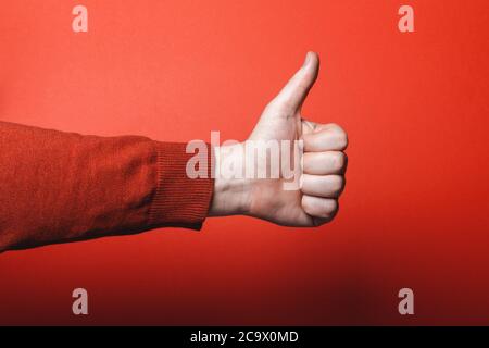La main de l'homme montre le pouce vers le haut sur fond rouge. Banque D'Images
