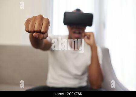 Jeune homme noir enthousiaste dans le casque de réalité virtuelle jouant au jeu de combat Banque D'Images