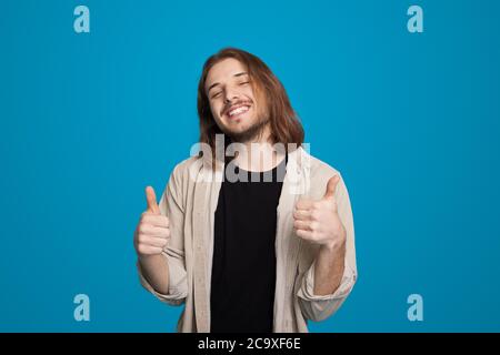 Long homme d'affaires à poil long gestant le signe de la publicité comme quelque chose sur le mur bleu de studio Banque D'Images