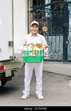 Portrait d'un beau jeune coursier vietnamien tenant une caisse en plastique avec des bouteilles de lait, du pain frais et des fruits Banque D'Images
