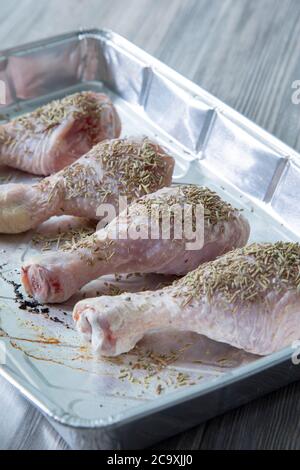 Cuisses de pilon de poulet crumstick crues recouvertes de romarin dans une plaque de cuisson en aluminium Banque D'Images