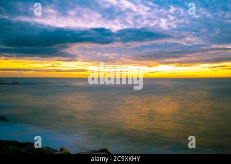 Coucher de soleil sur une eau douce et soyeuse avec reflets colorés - paysage marin à longue exposition avec espace de copie Banque D'Images