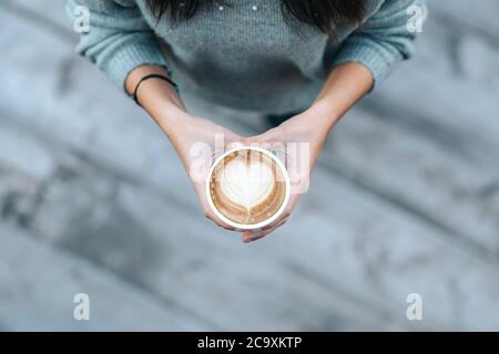 Jeune femme tenant une tasse jetable avec un café en forme de cœur dans un café. Photo de haute qualité Banque D'Images