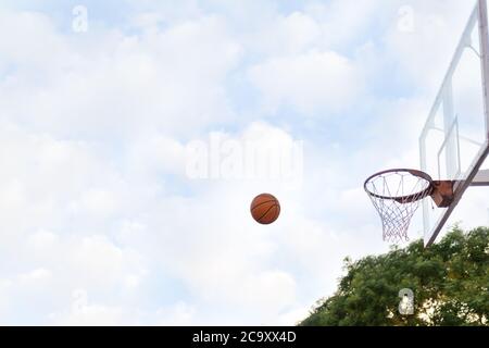 Le ballon s'envole dans le panier de basket-ball. Vue latérale. Ciel avec nuages en arrière-plan. Concept de jeux sportifs. Banque D'Images