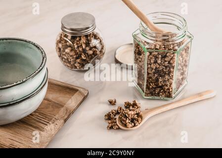 Granola maison saine et nourrissante pour le petit déjeuner de keto dans des pots en verre avec des cuillères en bois et des bols en céramique bleue sur table de cuisine en marbre Banque D'Images