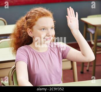 Une écolière lève la main dans une classe d'école primaire Banque D'Images