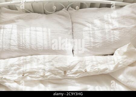 Belle lumière du matin dans la chambre. Literie blanche aux couleurs pastel. Linge de lit bio tendance en lin naturel. Intérieur confortable. Banque D'Images