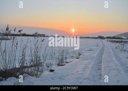 Coucher de soleil en hiver avec des impressions de pneus de voiture dans la neige. Banque D'Images