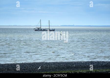 Harlingen,pays-Bas,juillet 23,2020:Wadden mer avec planche à voile et vieux voilier traditionnel, digue en pierre noire, jetée et à l'horizon Banque D'Images