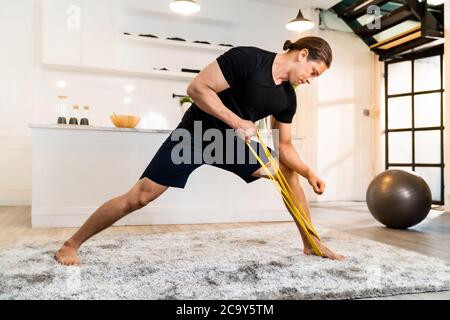 White caucasien FIT sportif musclé homme faisant l'exercice avec le groupe d'étirement dans le salon à la maison pour la santé mentale et la méditation. Pour travailler Banque D'Images