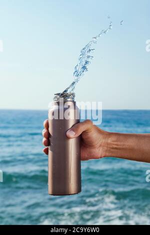 gros plan d'un homme qui verse de l'eau dans une bouteille d'eau réutilisable en aluminium devant l'océan Banque D'Images