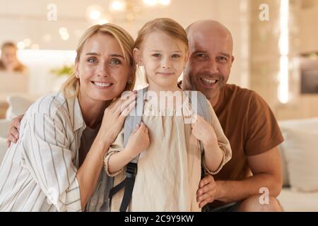 Portrait aux tons chauds d'une famille heureuse qui regarde l'appareil photo et sourit tout en posant avec un joli sac à dos de petite fille Banque D'Images