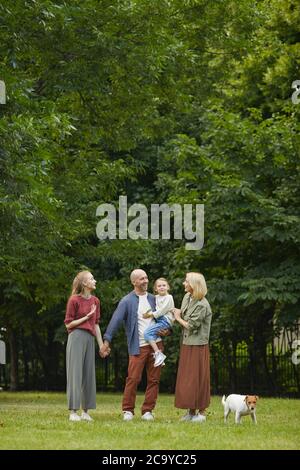 Portrait vertical grand angle de la famille insouciante avec deux enfants et un chien debout sur l'herbe verte à l'extérieur tout en appréciant une promenade dans le parc ensemble, espace de copie Banque D'Images