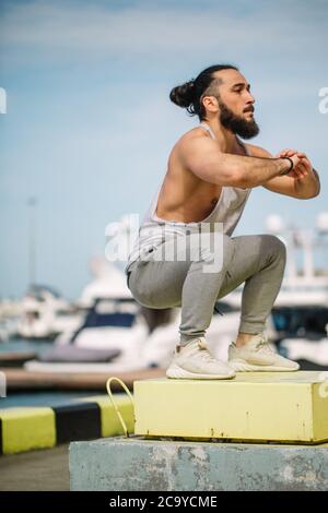 Entraînement de fitness Extreme Jump Squats. CrossFit athlète homme caucasien faisant High Jump squat entraînement sur une boîte de fortune à la marina d'été jetée Banque D'Images