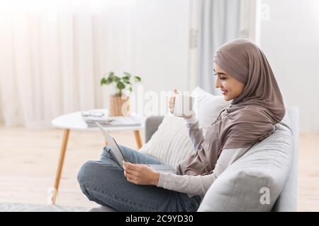 Style de vie domestique. Femme musulmane se détendant à la maison avec un ordinateur portable et du café Banque D'Images