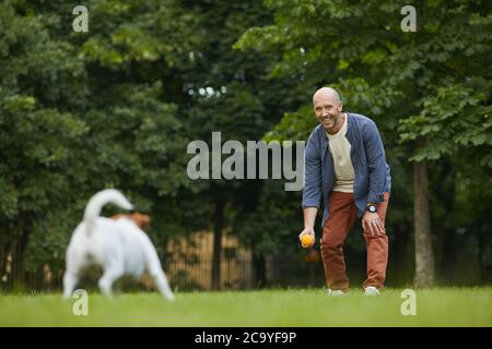 Portrait complet d'un homme mûr souriant jouant avec un chien dans le parc, jetant le ballon sur l'herbe verte et s'amusant avec un animal de compagnie, espace de copie Banque D'Images