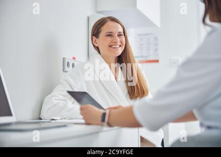 Femme en train de rire portant un peignoir blanc doux discutant avec un médecin Banque D'Images