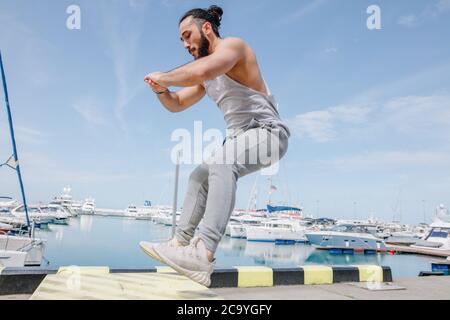 Entraînement de fitness Extreme Jump Squats. CrossFit athlète homme caucasien faisant High Jump squat entraînement sur une boîte de fortune à la marina d'été jetée Banque D'Images