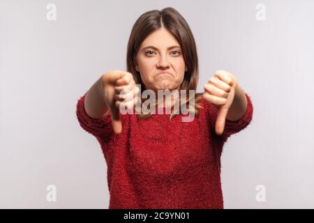 Service horrible ! Portrait d'une fille mécontente dans un chandail déchiquable montrant les pouces doubles et grimaquant avec le dégoût, exprimant la désapprobation, mauvaise feedba Banque D'Images