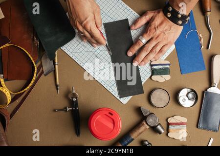 Outils et équipement pour les articles faits à la main en cuir. Image rognée d'un artisan masculin faisant sur mesure un portefeuille de conception pour un nouveau client à son atelier. Lea Banque D'Images