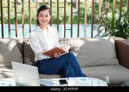 Portrait d'une jeune femme d'affaires asiatique heureuse remplissant le planificateur et regardant l'appareil photo Banque D'Images