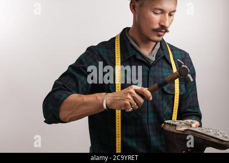 Portrait d'un cordonnier avec un ruban à mesurer, en collaboration avec d'un cordonnier Man working with leather boot à l'aide de l'élaboration d'un marteau, isolé tourné pendant Banque D'Images