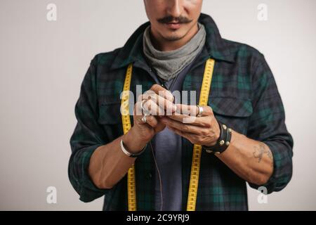 Image rognée d'un cordonnier avec moustache et ruban de mesure enfilant l'aiguille sur fond blanc. Petites entreprises et fabrication de main, L Banque D'Images