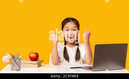 Une jeune fille coréenne joyeuse au PC portable secouant les poings sur fond jaune Banque D'Images