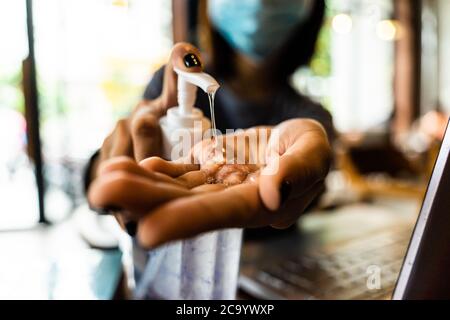 Jeune femme se lavant les mains avec du gel d'alcool en quarantaine pour le coronavirus portant un masque de protection avec distanciation sociale et utilisant le travail d'ordinateur portable Banque D'Images