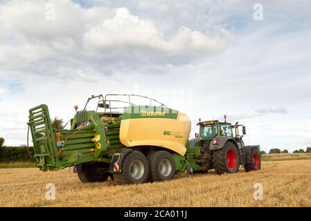 Vue arrière d'un tracteur utilisant une presse à balles de foin dans un champ. Beaucoup Hadham, Hertfordshire. ROYAUME-UNI. Banque D'Images