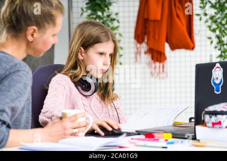 Jeune fille blonde dans le chandail rose est confondue en faisant ses leçons. Sa mère l'aide. Homeschooling pendant l'isolement à la maison. Banque D'Images