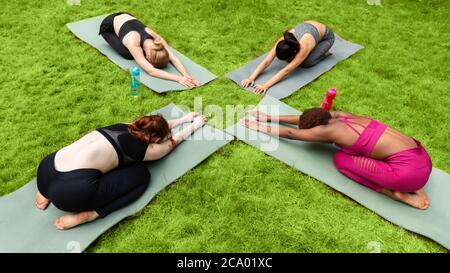 Groupe de filles diverses exécutant la pose d'enfant pendant leur cours de yoga à l'extérieur Banque D'Images