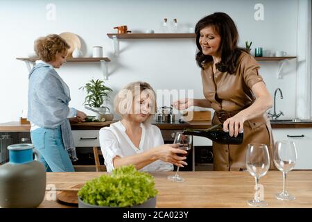 Belle dame de Brunette qui verse du vin au verre de son vieil ami à la cuisine moderne. Les femmes se sont rencontrées pour préparer leur repas. Vivre la vie entière à tout âge Banque D'Images