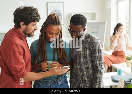 Portrait à taille haute d'un groupe multiethnique de personnes regardant l'écran du smartphone tout en étant debout au bureau, espace de copie Banque D'Images