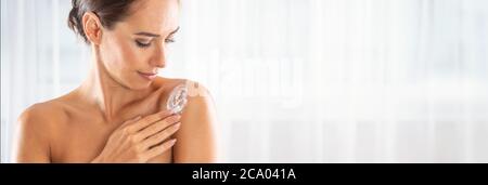 Belle jeune femme appliquant de la crème sur son épaule. Concept de bien-être et de cosmétiques pour les soins de la peau. Banque D'Images