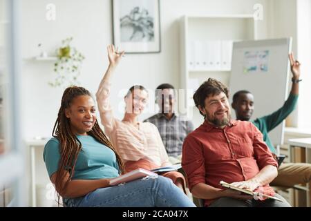 Groupe multiethnique de personnes levant la main tout en répondant à des questions lors d'un séminaire de formation ou d'une conférence d'affaires au bureau, dans un espace de copie Banque D'Images