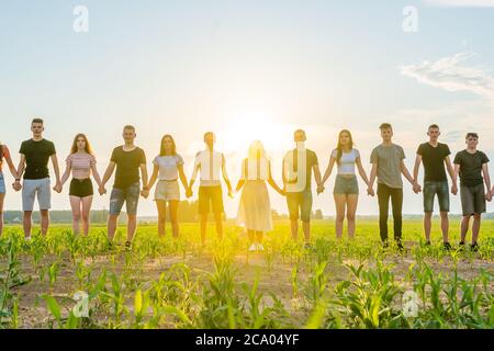 Concept de cohésion. Un groupe d'amis se tient les mains au coucher du soleil. Banque D'Images