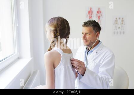 un médecin de sexe masculin avec une barbe de trois jours examine une jeune fille avec un stéthoscope Banque D'Images