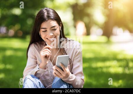 Liste de lecture favorite. Asian Girl avec son smartphone écouter de la musique tout en se détendant dans Park Banque D'Images
