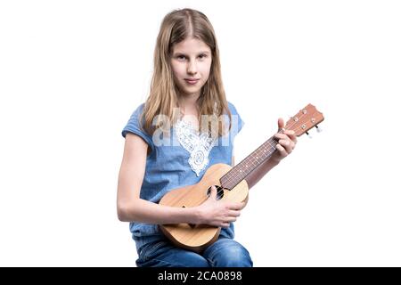 Jeune fille blonde en T-shirt bleu joue en concert sur l'instrument ukulele. Banque D'Images