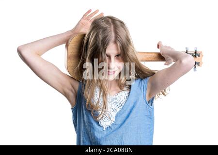 Adolescente, blonde en T-shirt bleu tient et joue l'instrument brun clair ukulele. Banque D'Images