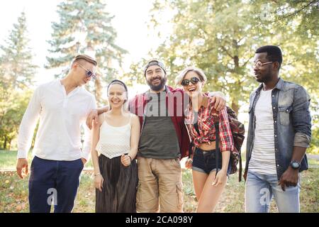 Groupe d'étudiants multiethniques vêtus de divers vêtements décontractés marchant au parc, sentant la joie et le bonheur. Amitié, intégration et con multiculturel Banque D'Images