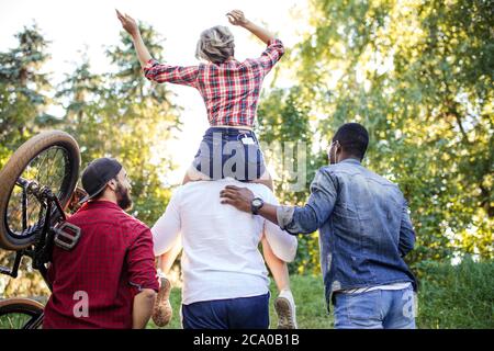 Arrière-face de race mixte méconnaissable divers jeunes qui vont au parc en été après-midi. Petit ami portant sa petite amie sur le porcgyback et Banque D'Images